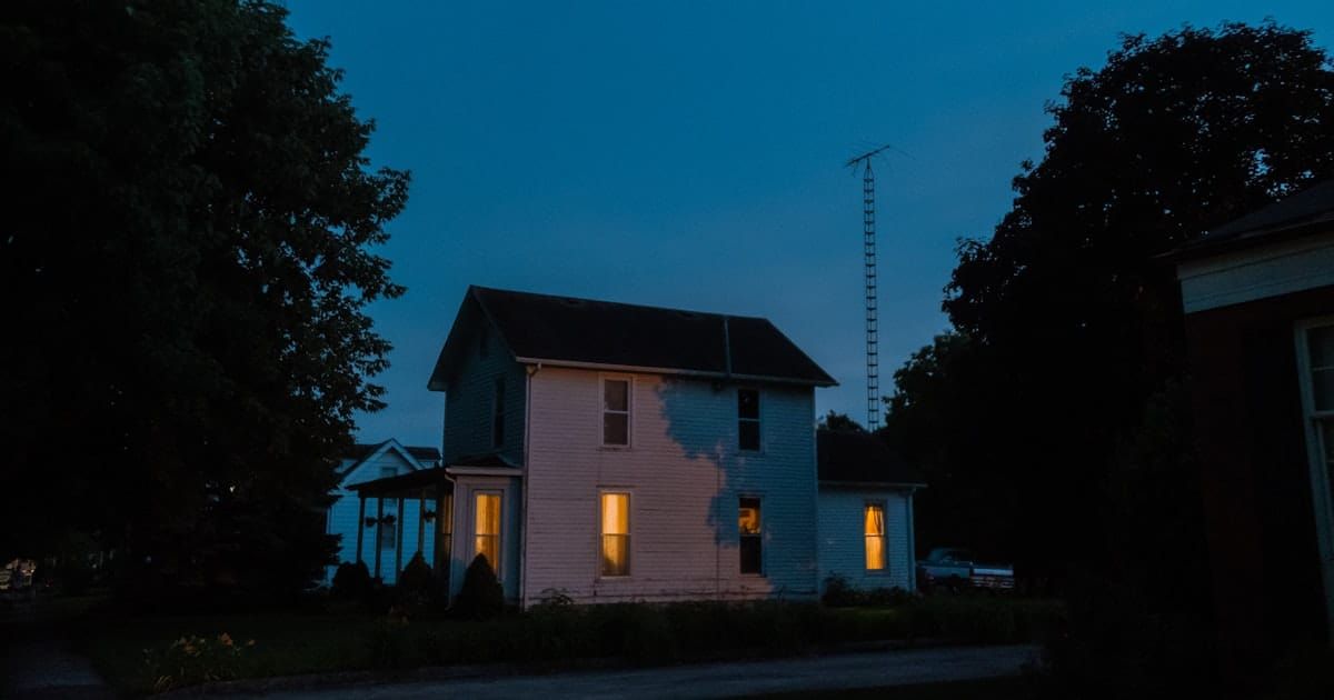 A house lit up at night with the interior lights on, seen from outside.