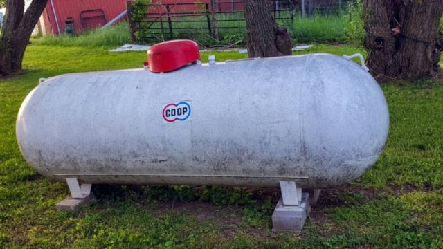 A white above-ground residential propane tank on concrete blocks in a grassy yard.