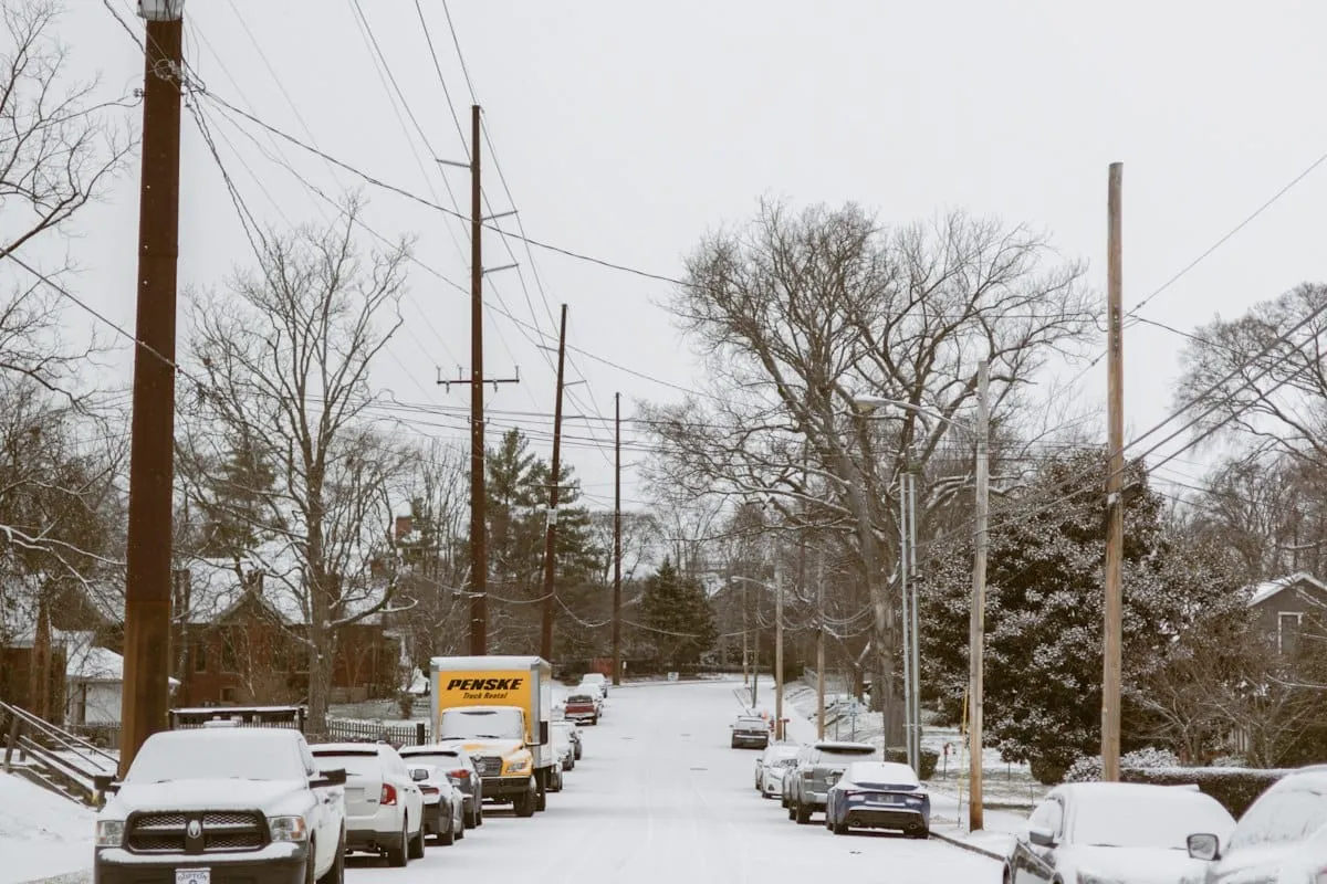 A snow covered street lined with power lines and parked cars.