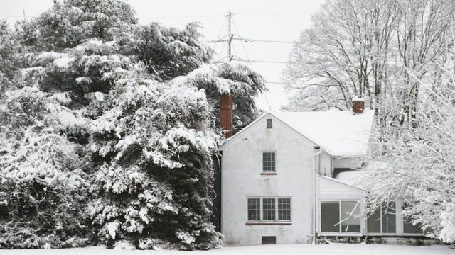 A white house and snow covered trees under power lines after a winter storm.