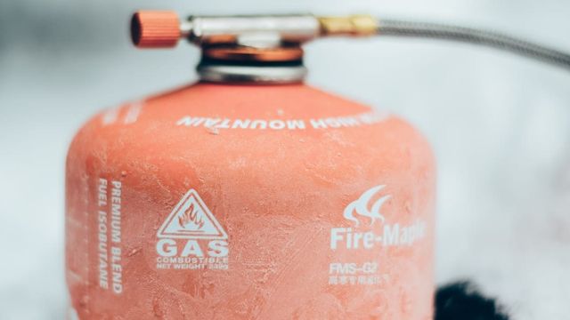 A red propane tank sitting on grass outdoors.