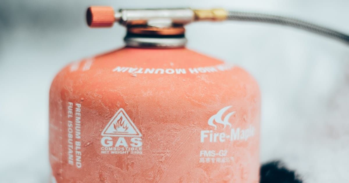 A red propane tank sitting on grass outdoors.