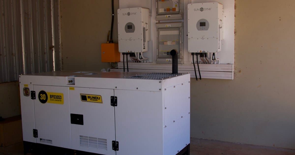 A white standby generator unit installed beside wall-mounted power equipment.